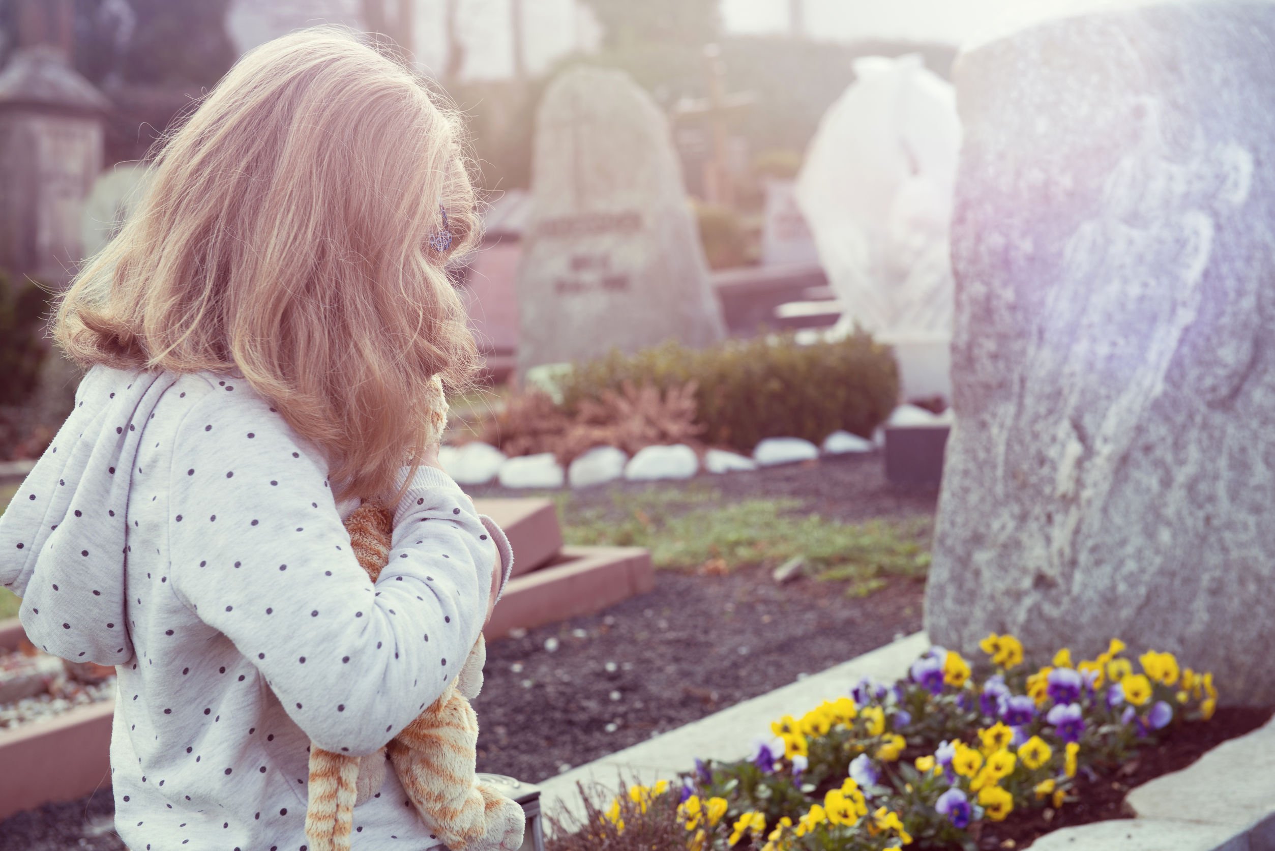 Menina diante do túmulo com flores.
