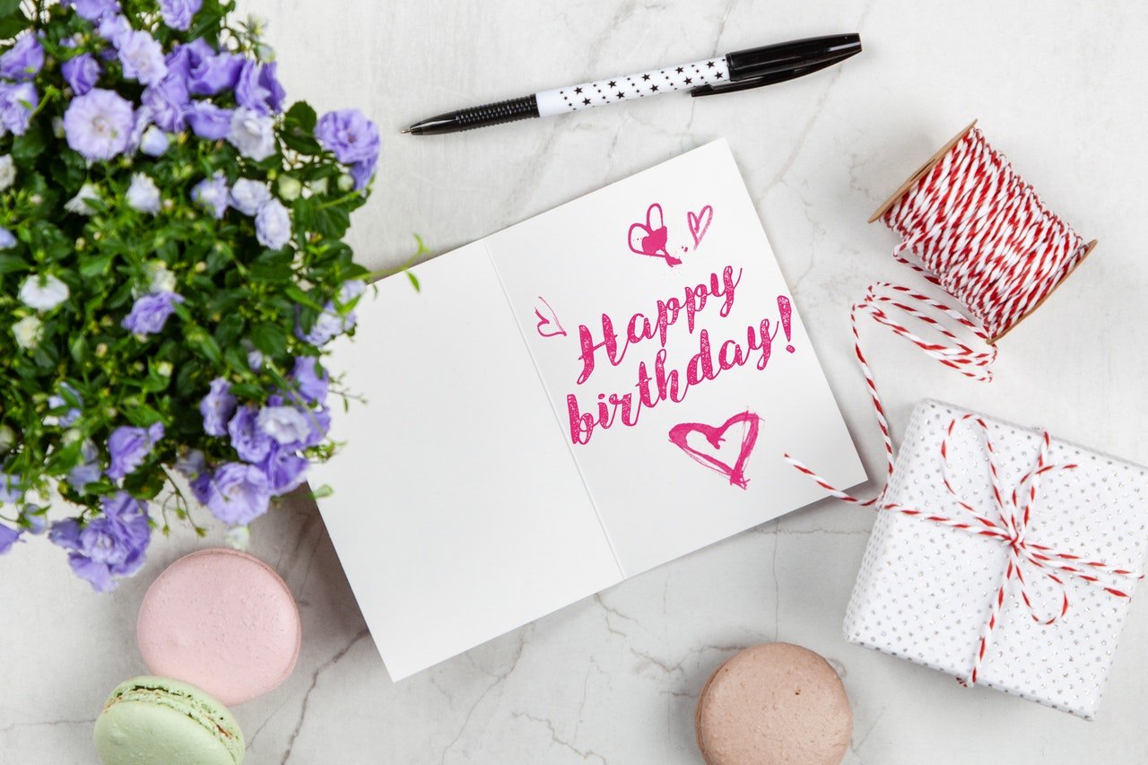 Mesa com flores, presentes e um caderno com os escritos: Happy Birthday!