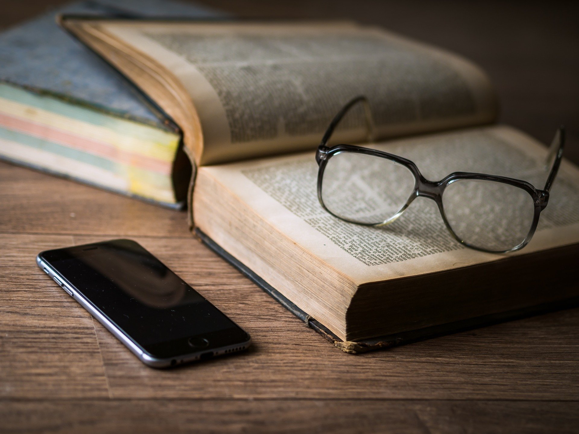 Foto de livro com óculos em cima e celular ao lado