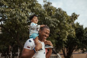 Filho criança nos ombros do pai, em um parque.