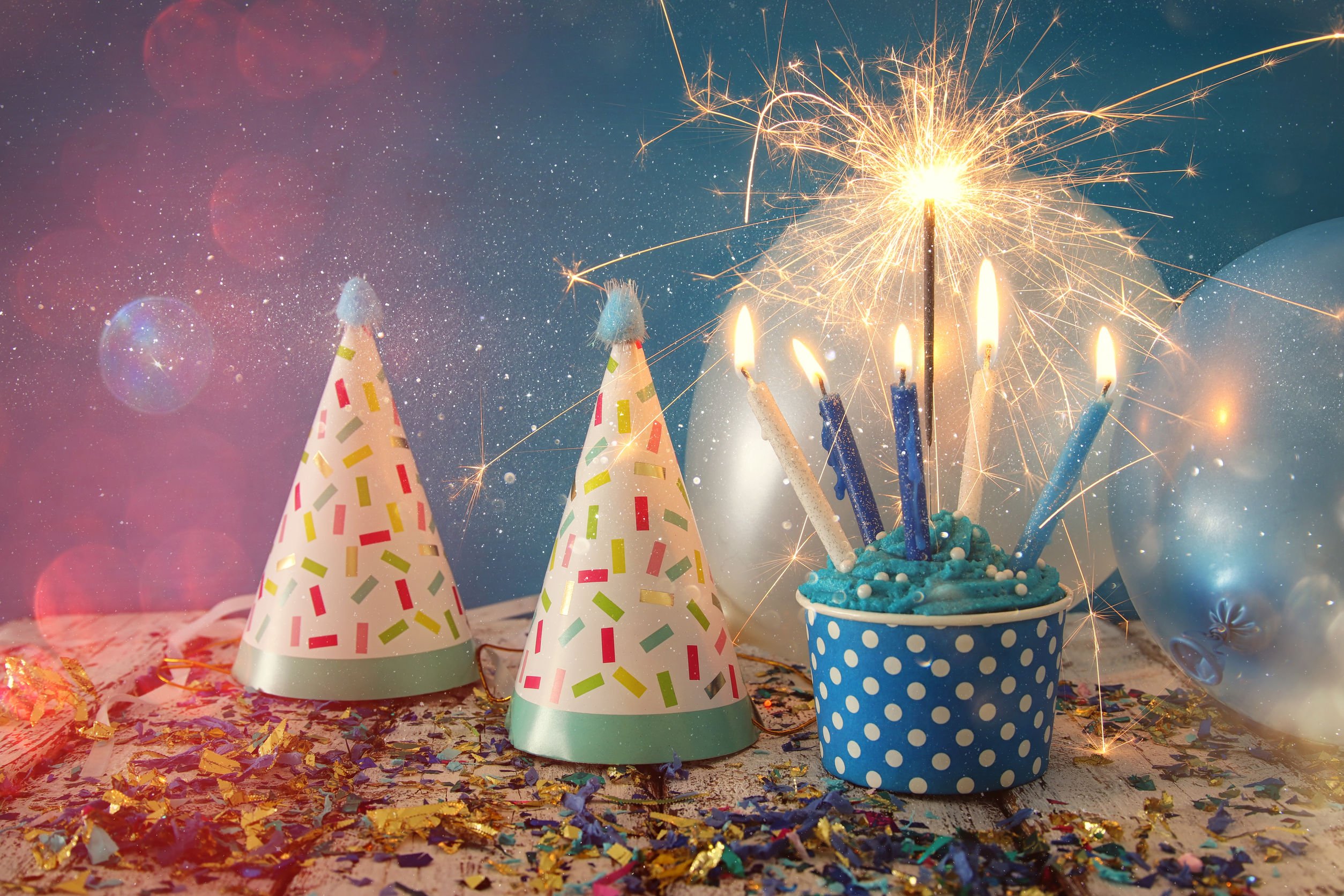 Chapéus, balões e um cupcake com velas acesas.