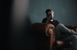 Homem sentando em sofá com mão no rosto triste