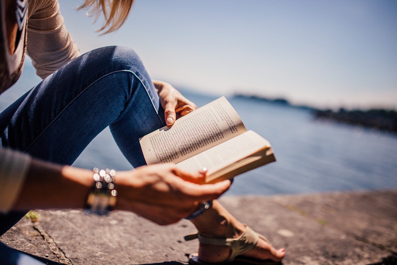 Mulher lendo um livro sentada de frente ao mar