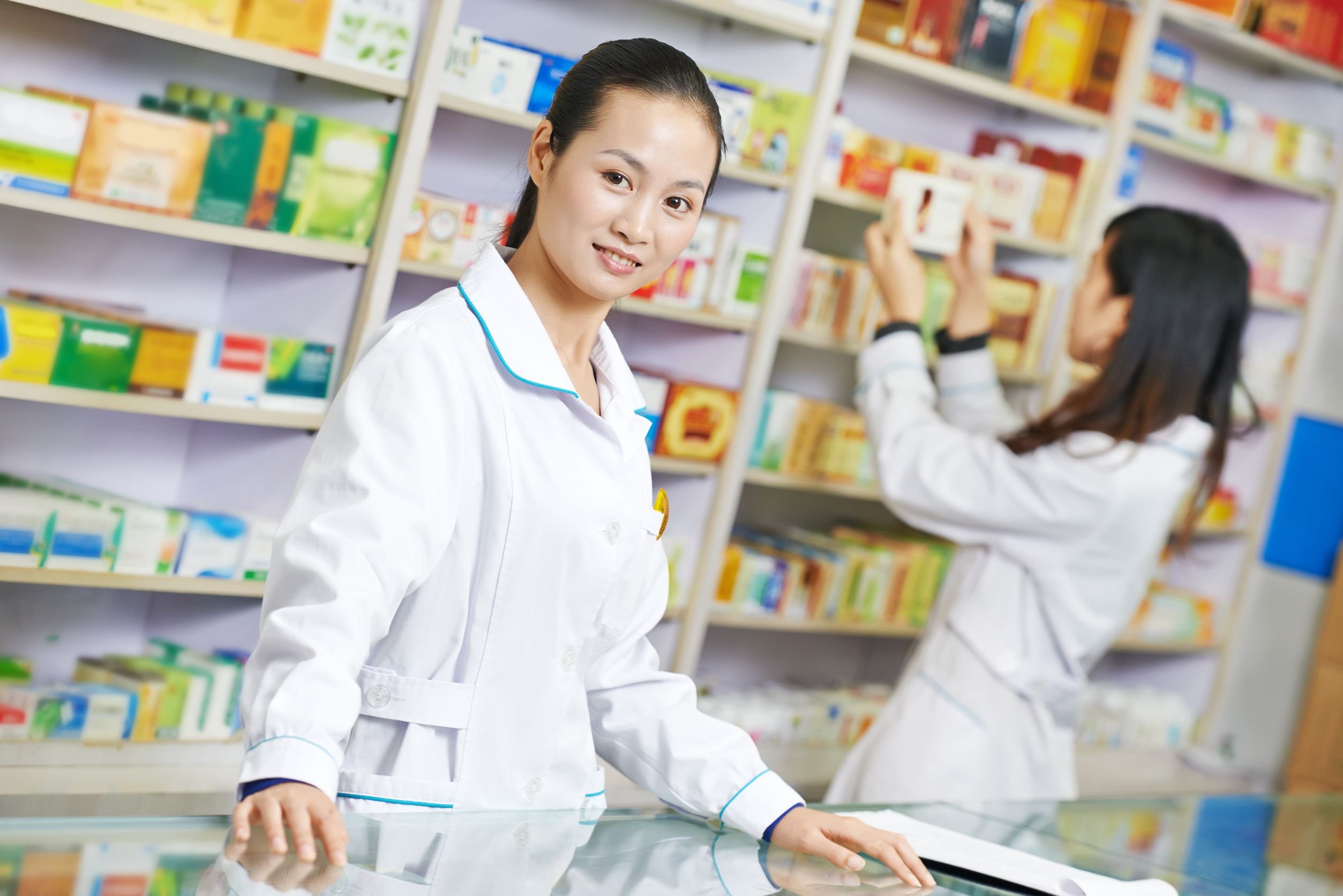 Farmacêutica sorrindo para a câmera atrás do balcão de uma farmácia.