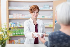 Farmacêutica sorri enquanto entrega um pequeno pacote para uma senhora idosa.