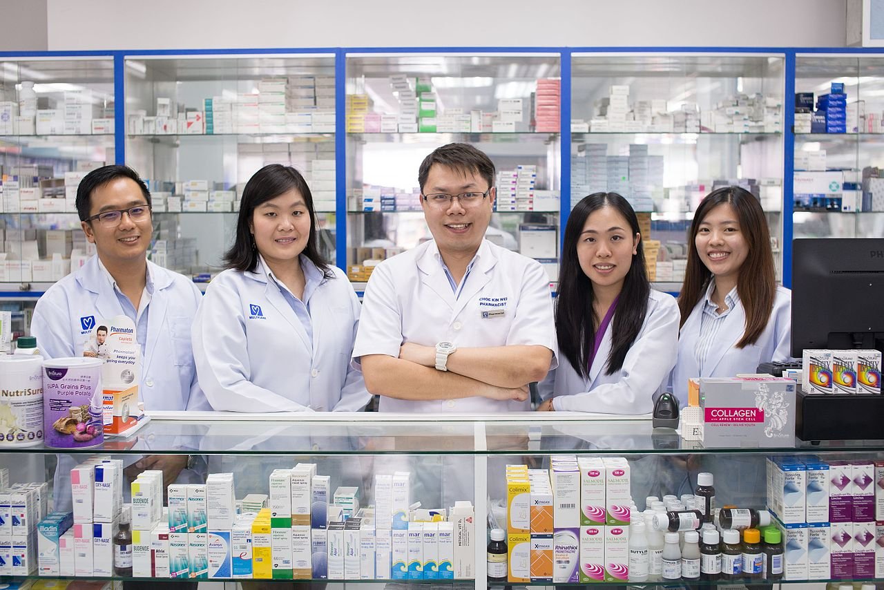 Equipe de cinco farmacêuticos na bancada de uma farmácia.