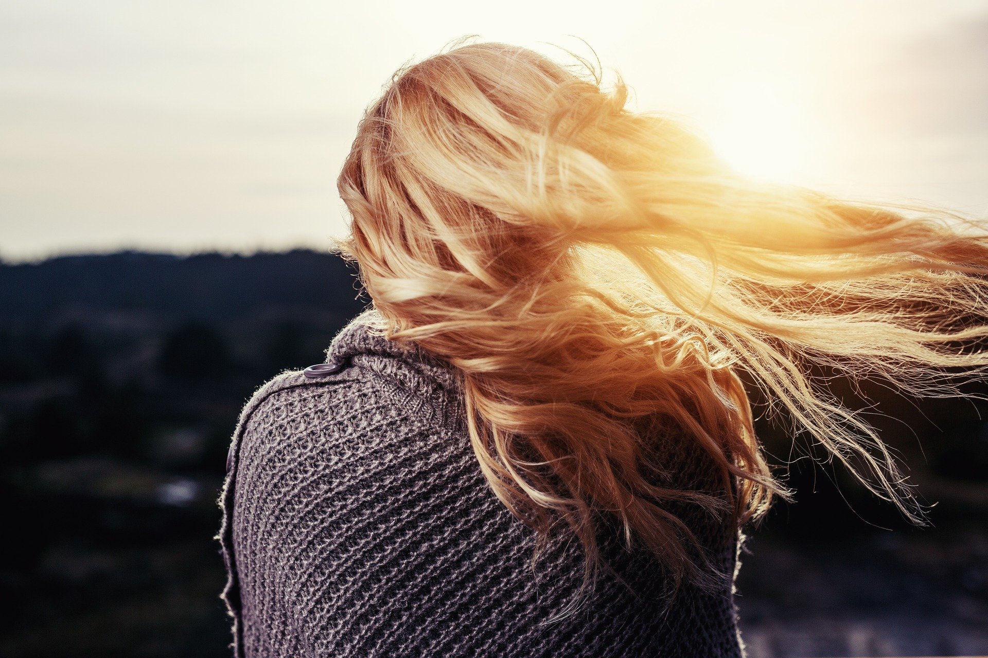 Mulher olhando em direção ao sol com cabelo esvoaçante