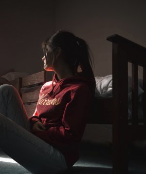 Mulher sentada no chão encostada na cama