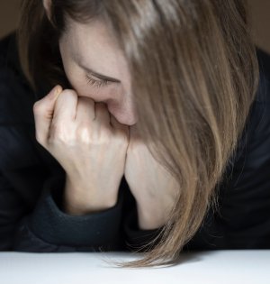 Mulher de cabeça baixa apoiando as mãos
