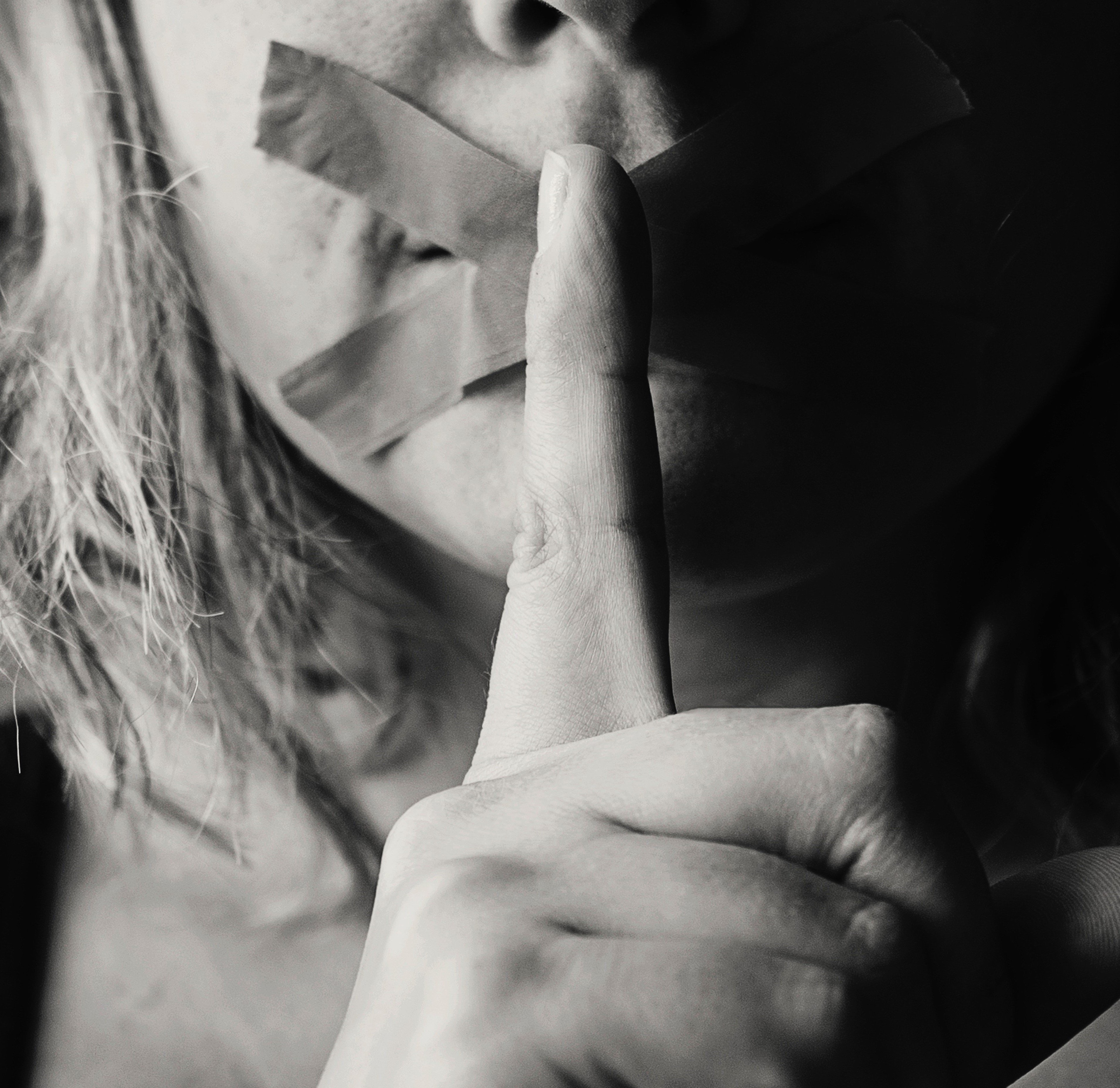 Mulher com a mão em frente a boca sinalizando silêncio