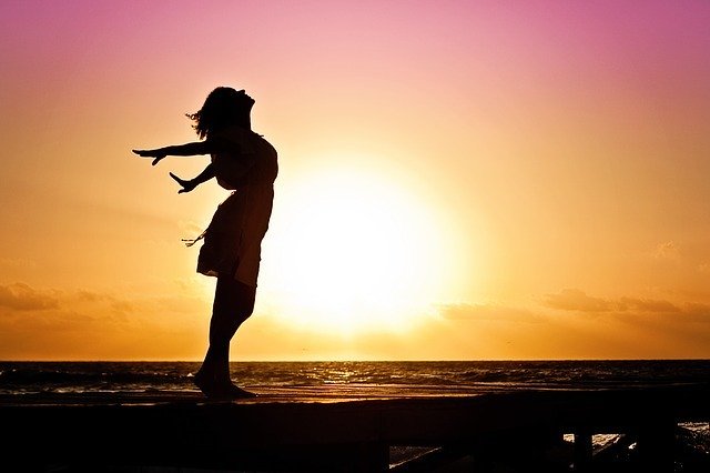 Silhueta de uma mulher com os braços abertos em frente ao sol