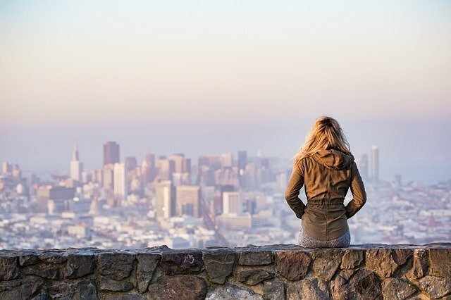 Mulher sentada em um muro com vista da cidade