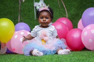 Bebê sentado com balões de aniversário em volta.