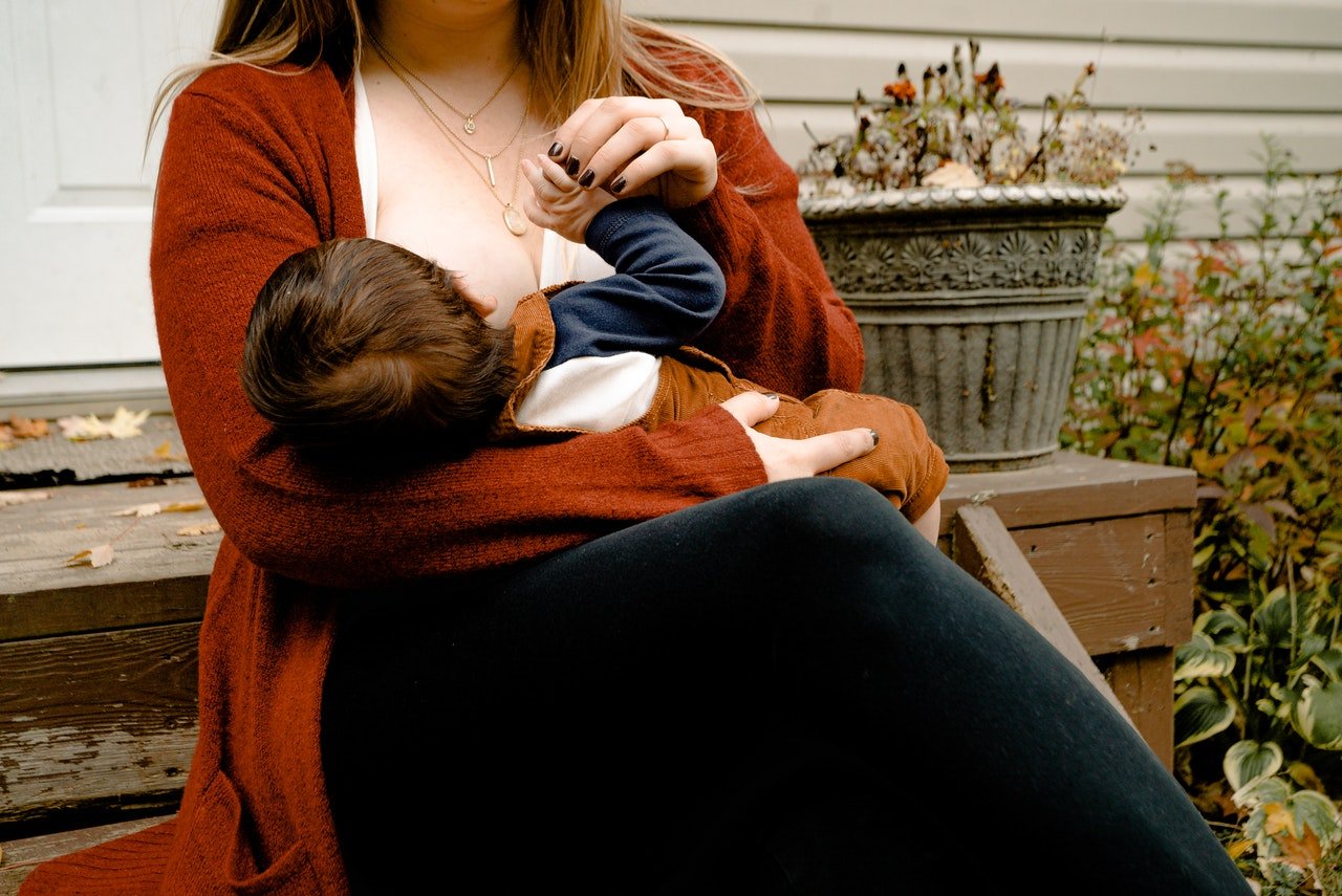 Mãe amamenta bebê enquanto segura em sua mão.