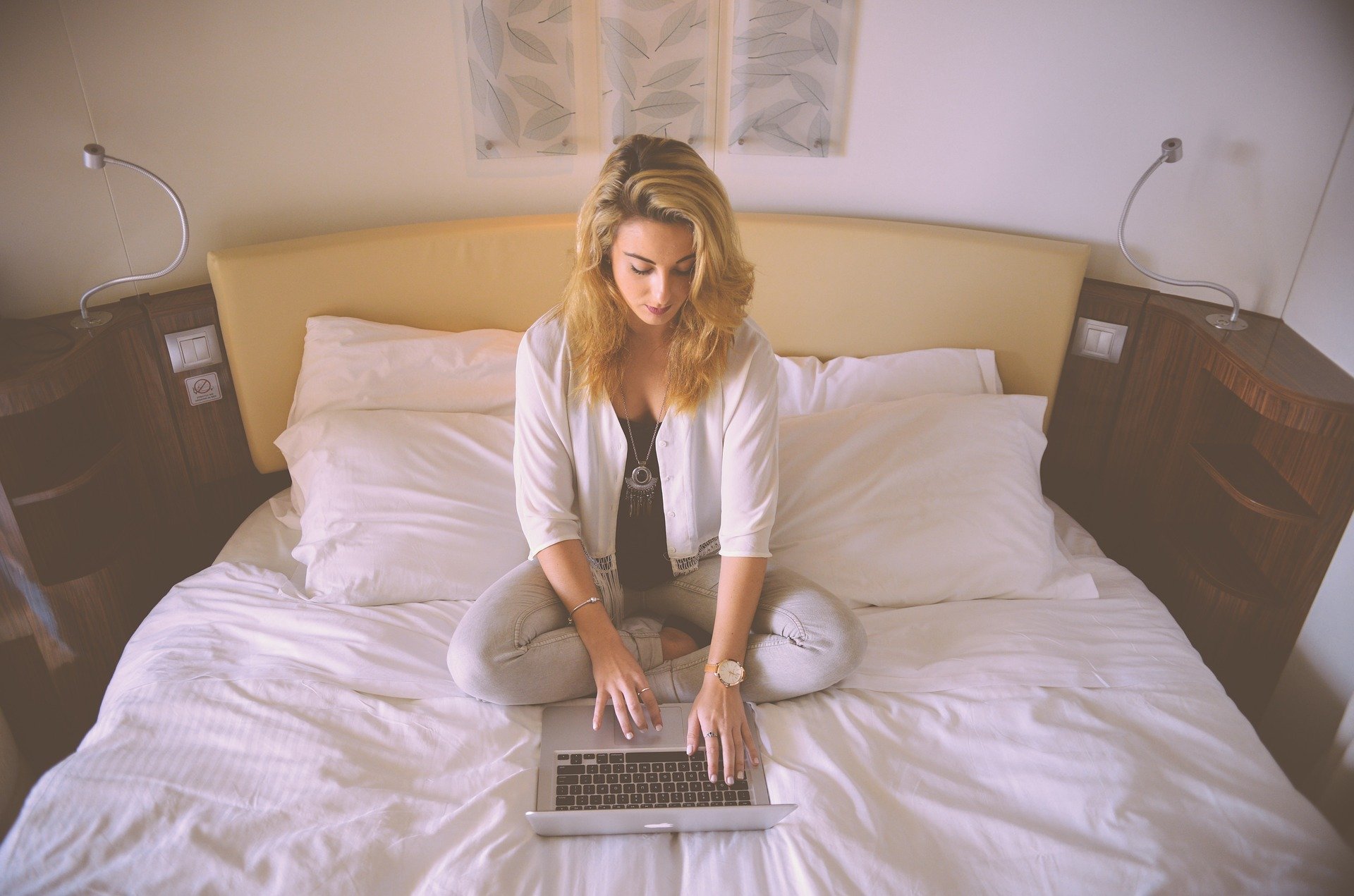 Mulher sentada na cama digitando no laptop