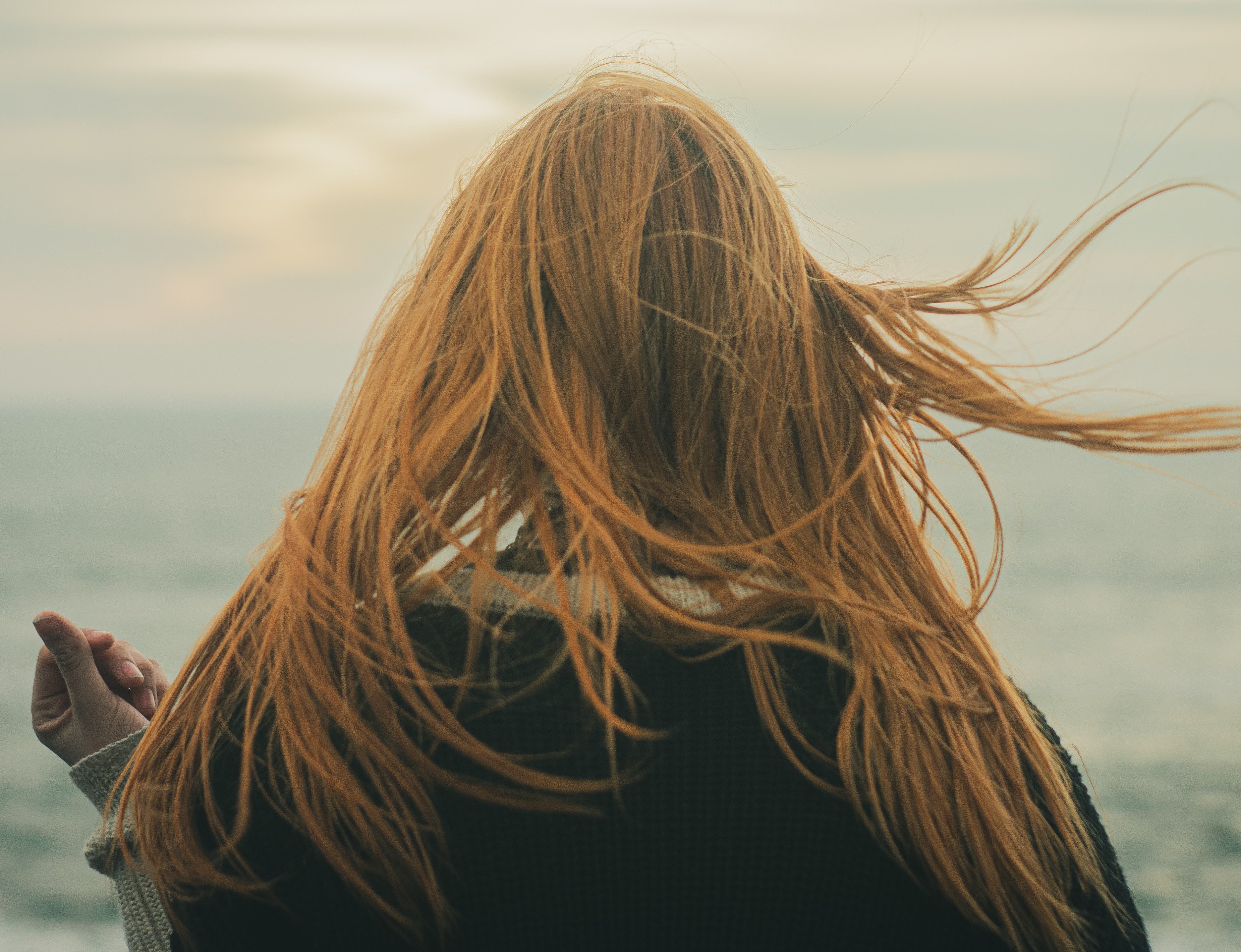 Mulher olhando para o mar com os cabelos ao vento
