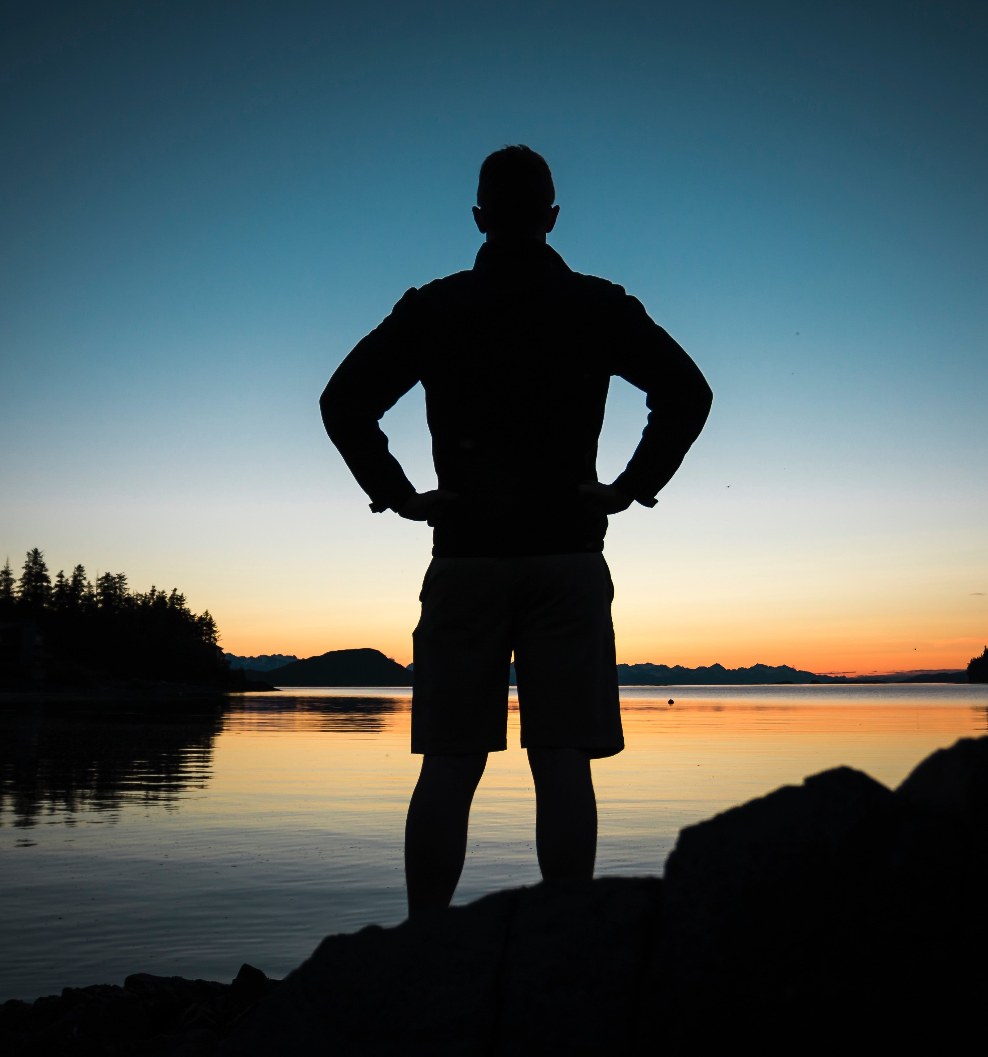 silhueta do homem em pé perto do mar durante o pôr do sol