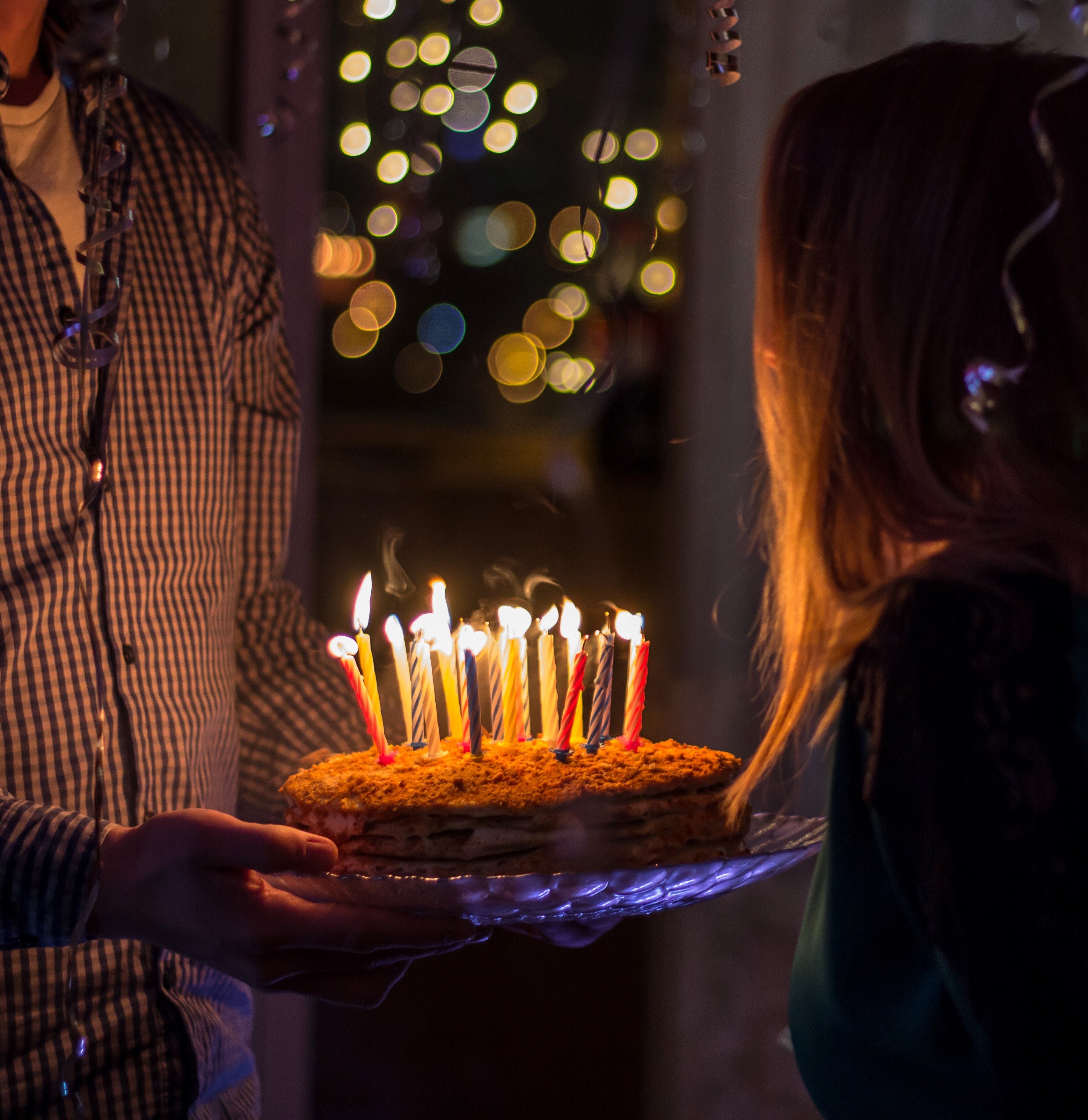 Pessoa segurando bolo com velas acesas e mulher de frente olhando para o bolo