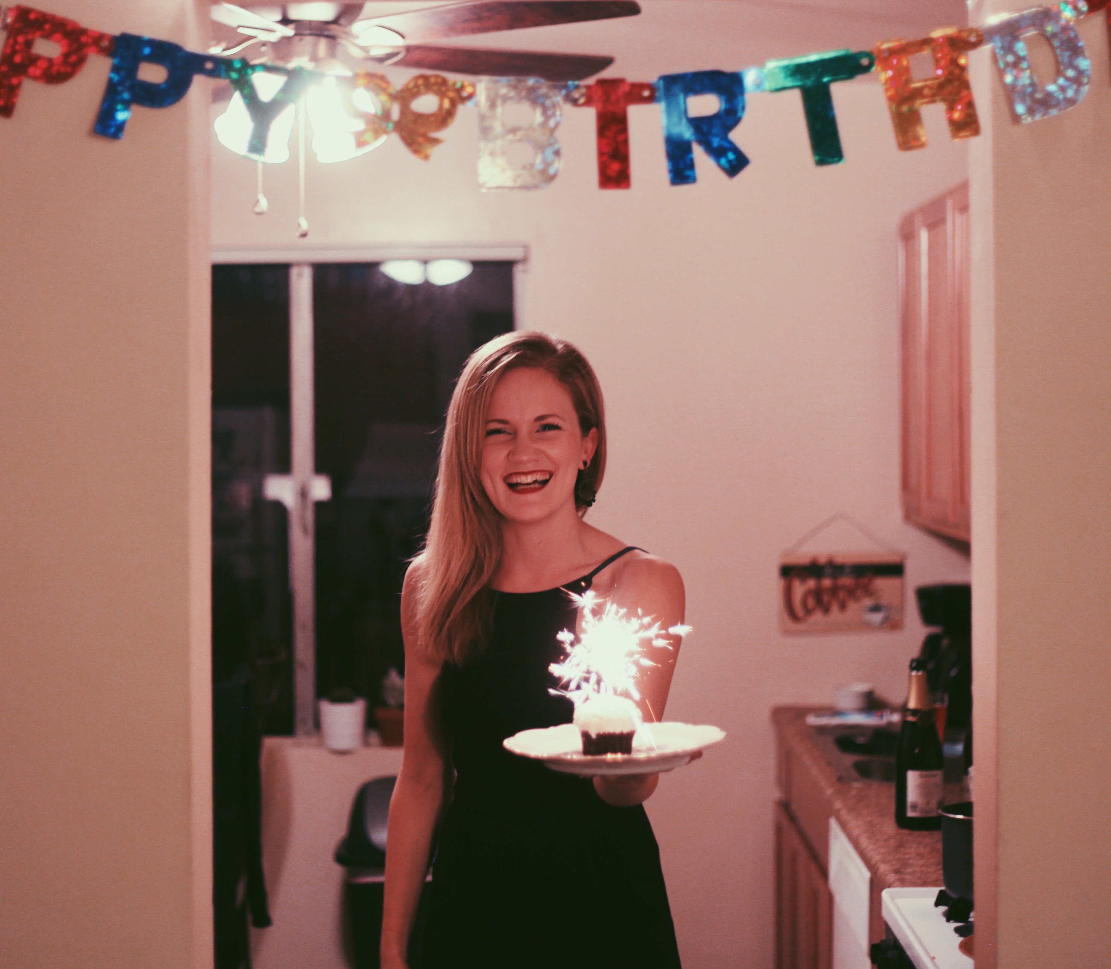 Mulher segurando bolo de aniversário e sorrindo, na cozinha