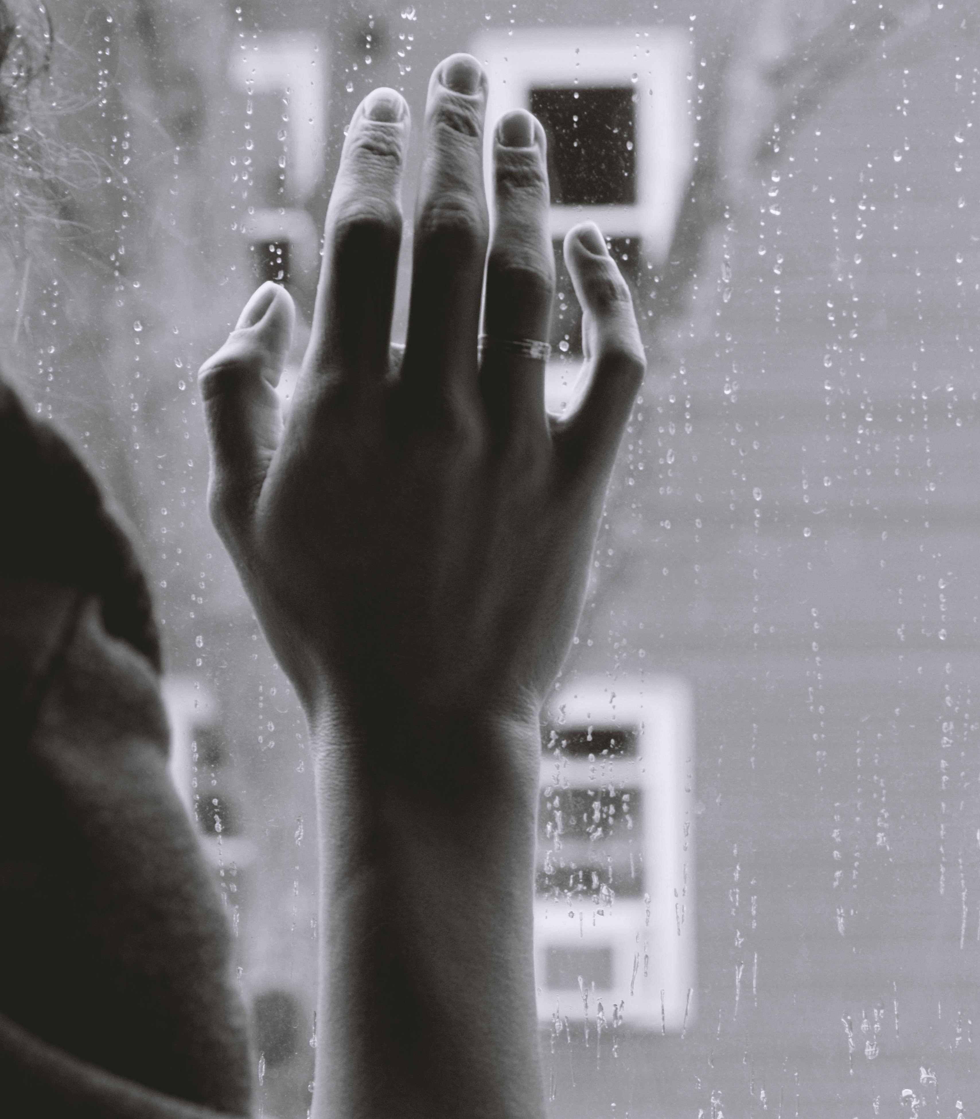 Mão na janela com gotas de chuva