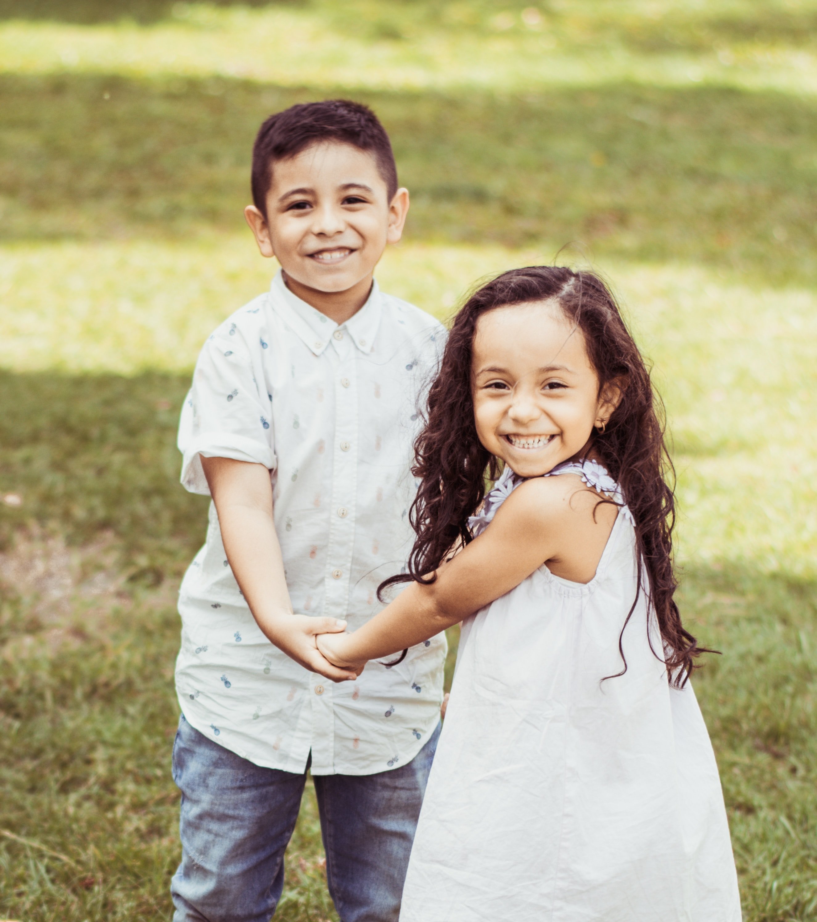 Menina e menino com as mãos dadas no gramado sorrindo