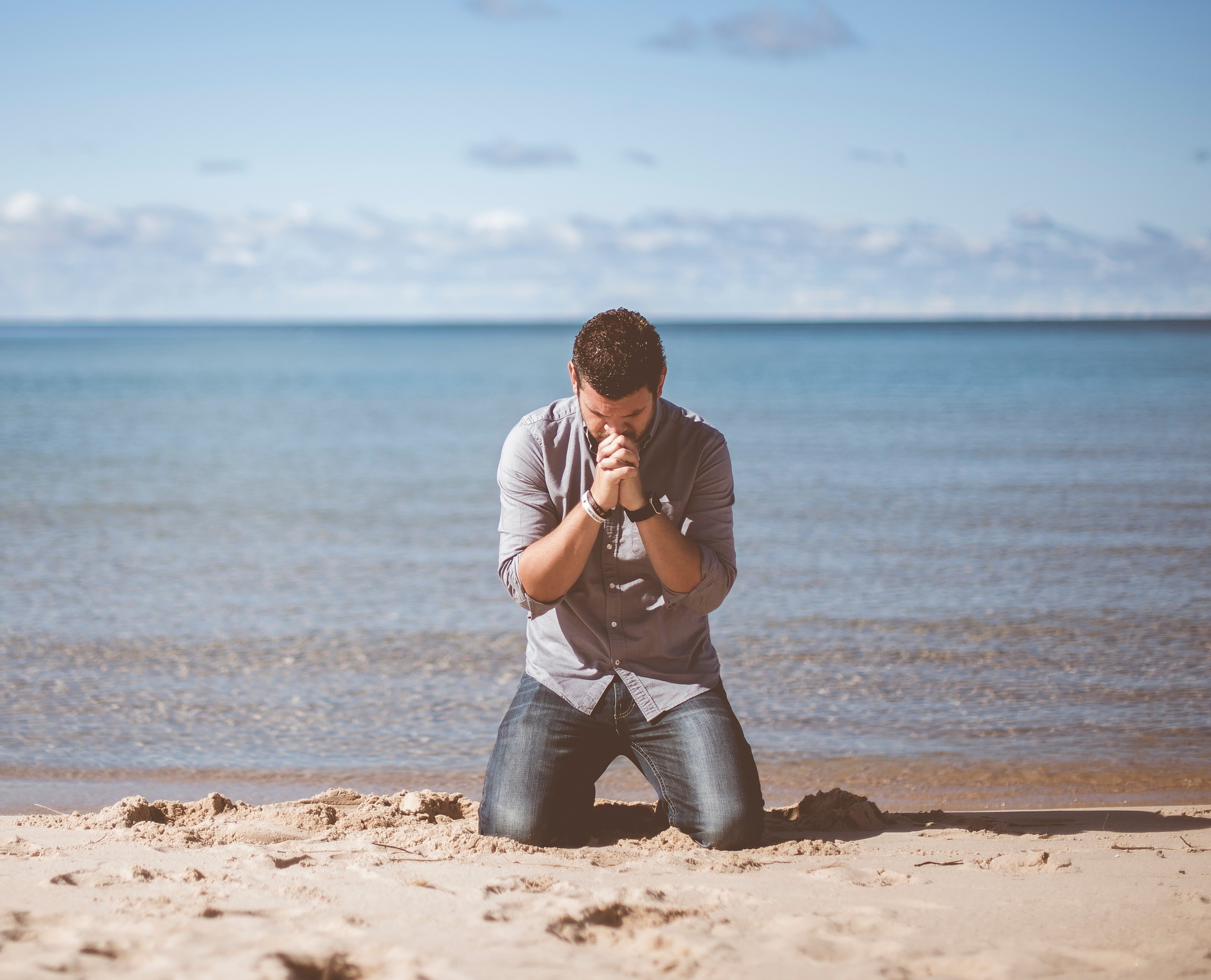 Homem ajoelhado rezando na praia