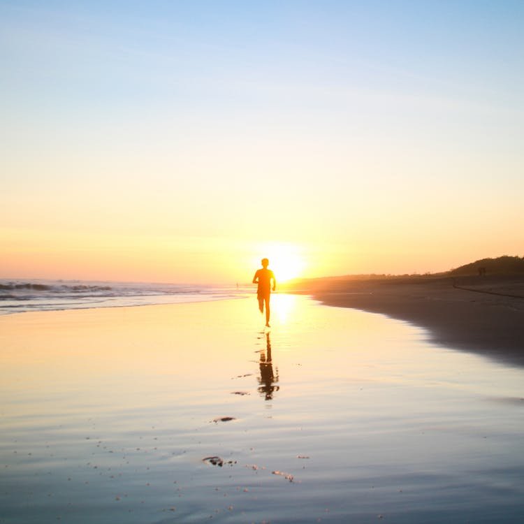 Homem caminhando na praia em direção ao sol