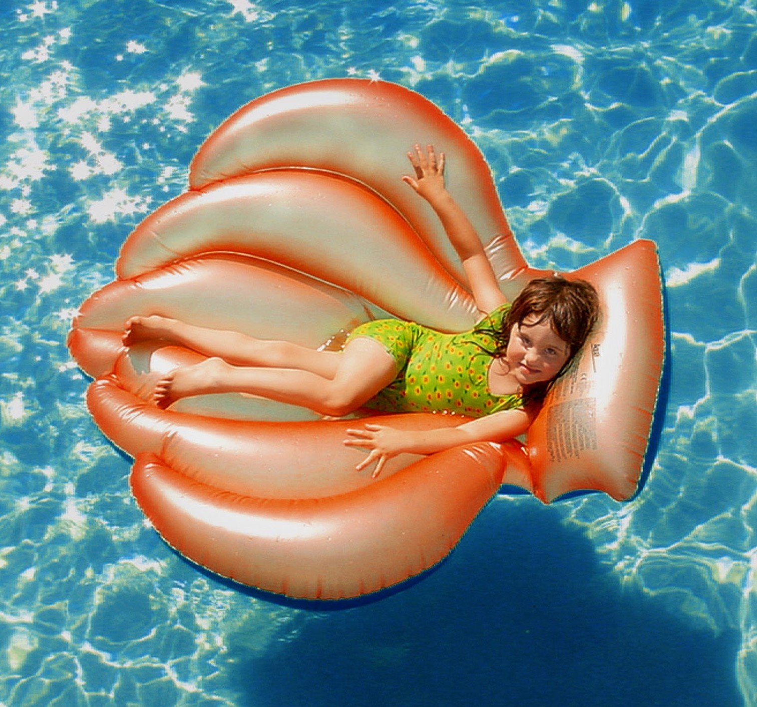 Criança deitada na boia de piscina em formato de concha