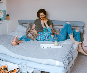 Casal deitado na cama comendo pedaço de pizza