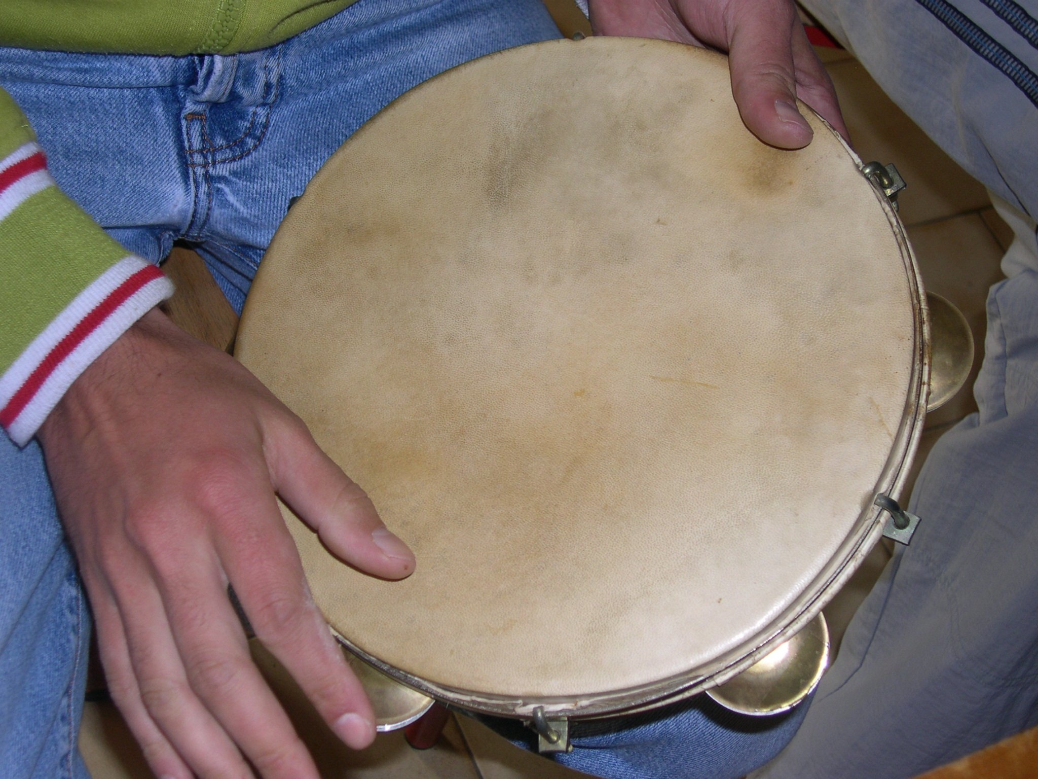 Pessoa tocando pandeiro, com o instrumento apoiado em sua perna esquerda.