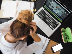 Mulher estressada com as mãos segurando o rosto em ambiente de trabalho.