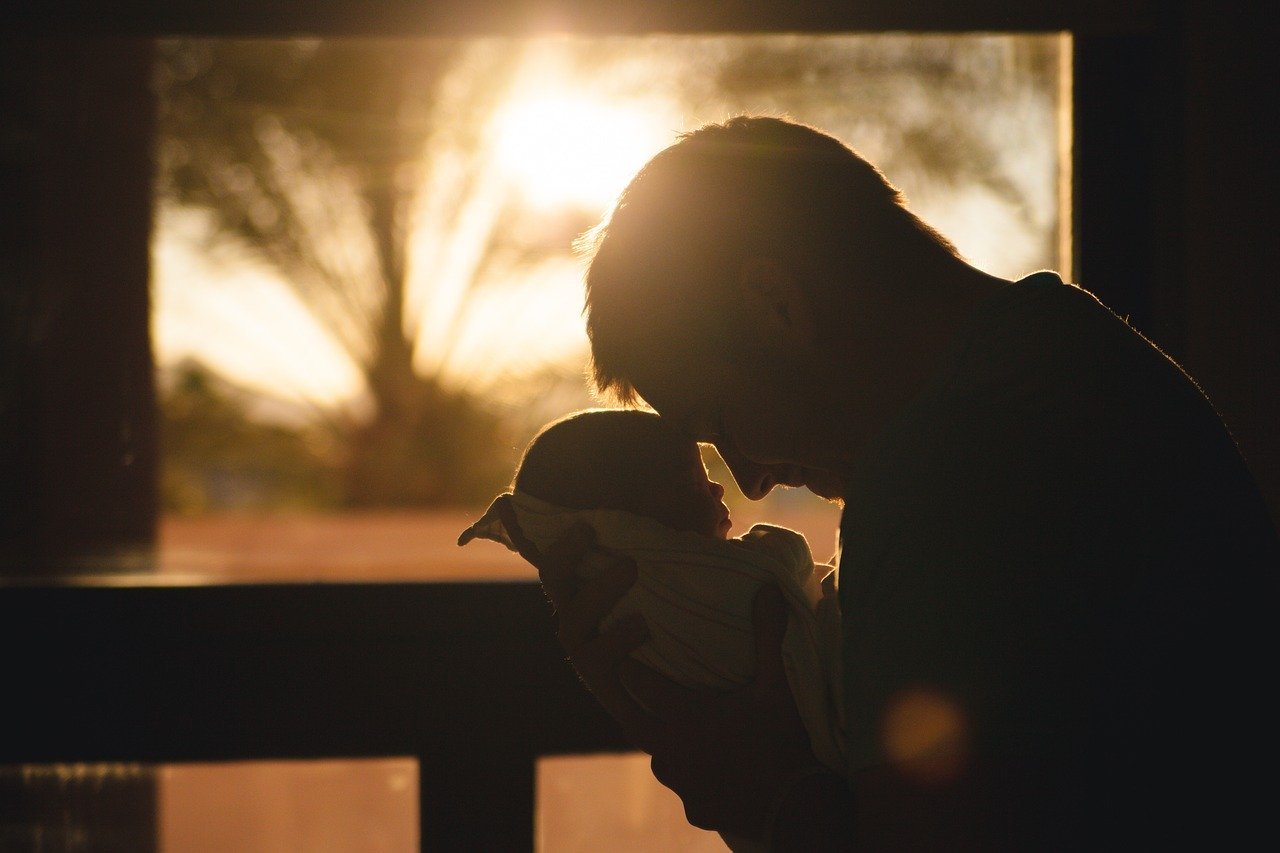 Silhueta de pai abraçando filho bebê ao pôr do sol.