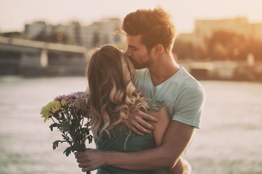 Namorado com flores beijando rosto de namorada