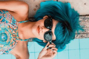 Mulher deitada na borda da piscina segurando óculos de sol no rosto