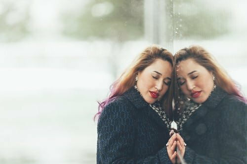 Mulher se apoiando em espelho de olhos fechados