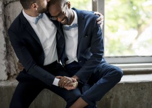 Casal de homens vestidos de terno e sorrindo.