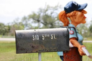 Boneco de carteira segurando uma carta ao lado de um caixa de correio.