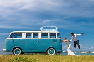 Mulher vestida de noiva empurrando um kombi e homem empurrando as costas da mulher