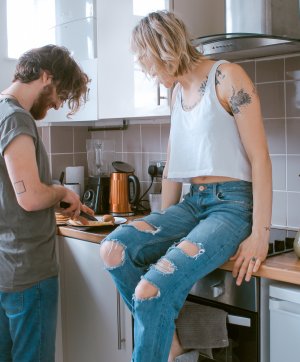 Mulher sentada no balção da cozinha e homem cortando algo