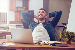 Homem na mesa do escritório com os braços na cabeça sorridente olhando para cima
