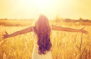 Mulher de braços abertos em campo com Sol batendo em seu rosto