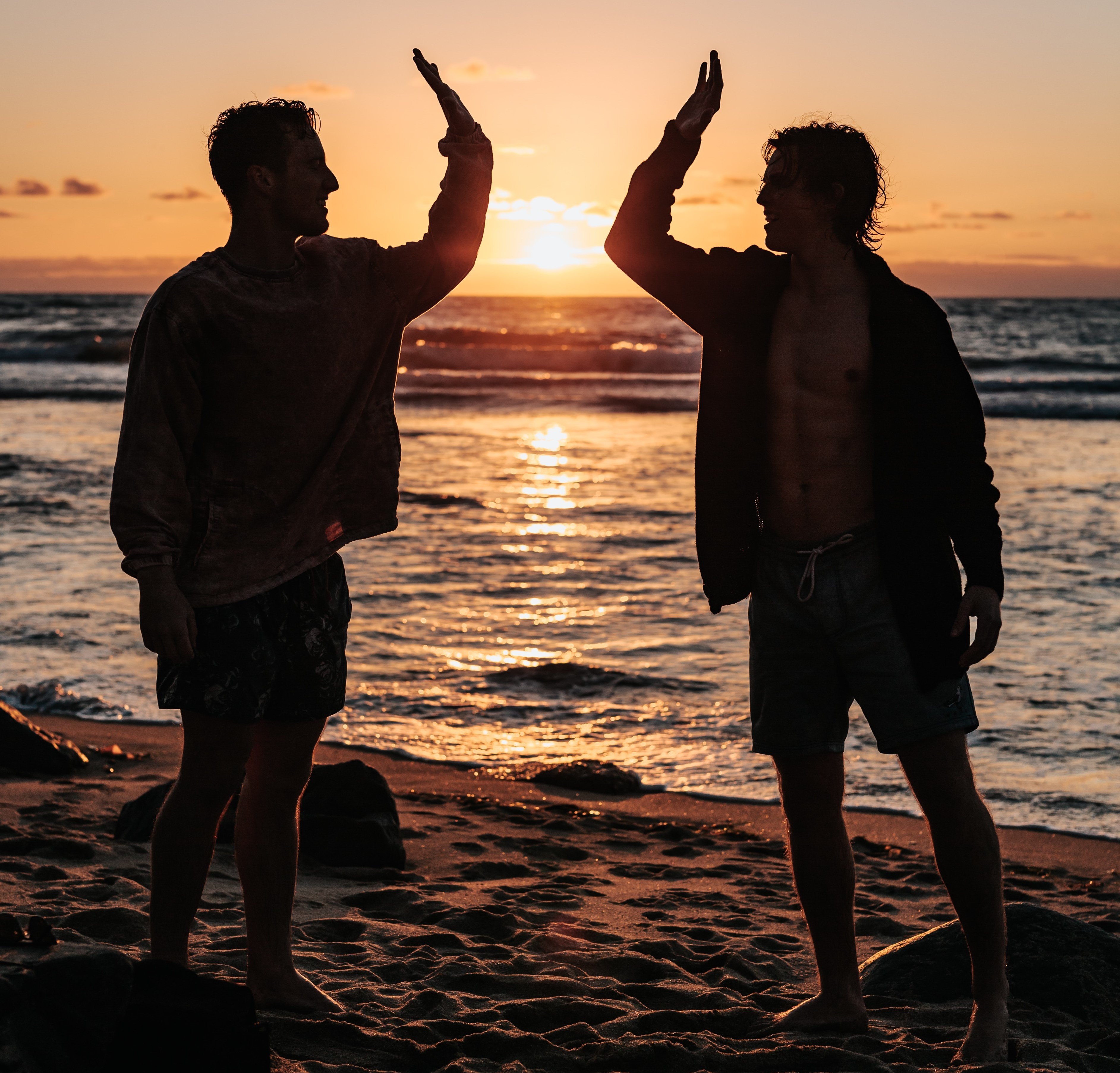 Dois homens na praia com o por do sol batendo as mãos