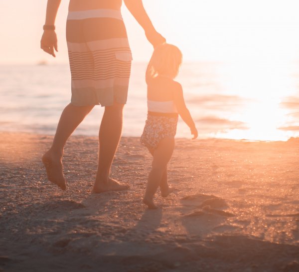 Homem de mãos dadas com criança na praia