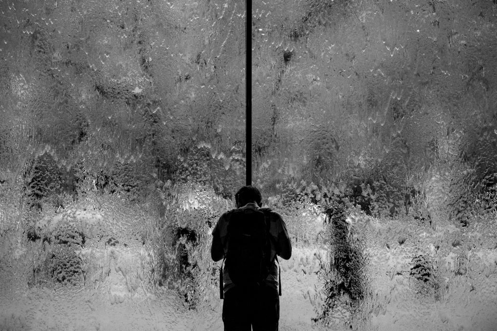Homem parado diante de vidro molhado.