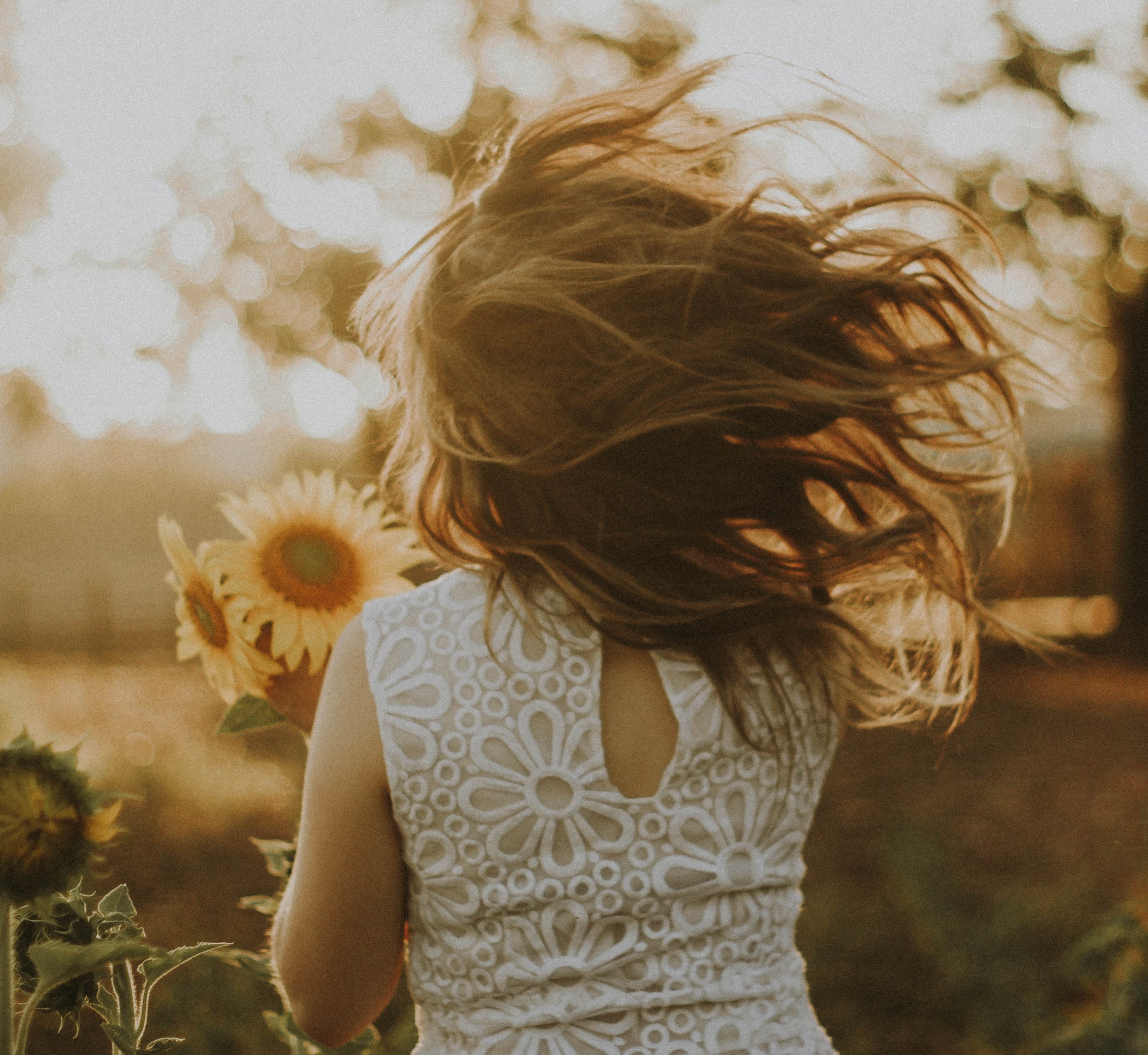 Menina segurando girassóis em um campo com os cabelos ao vento