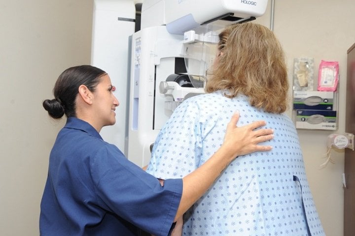 Uma técnica de mamografia auxiliando uma paciente durante a realização do exame.