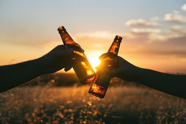 Duas pessoas brindando garrafas ao pôr do Sol