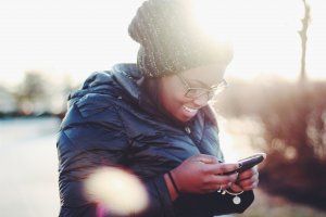 Unsplash - Meghan Schiereck Mulher usando o celular e sorrindo.