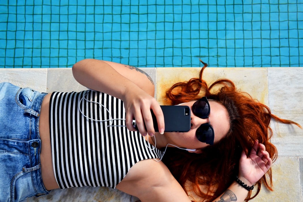 Mulher deitada na beira da piscina usando o celular.