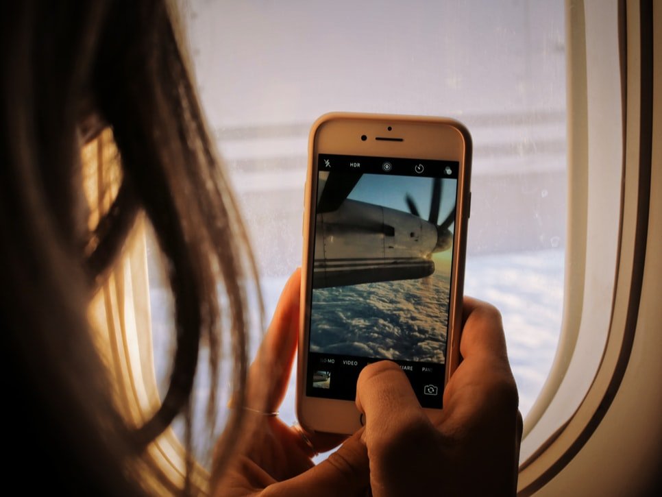 Mulher na janela de um avião tirando fotos.
